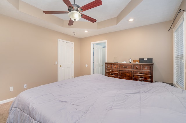 carpeted bedroom with a raised ceiling and ceiling fan