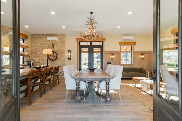 dining room with french doors, an inviting chandelier, light hardwood / wood-style flooring, and an AC wall unit