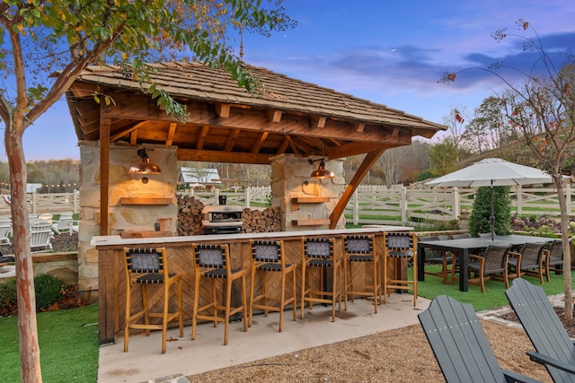 patio terrace at dusk with a stone fireplace, area for grilling, and a bar