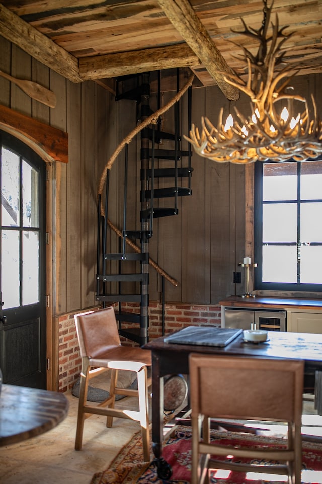 dining space with wood walls, a notable chandelier, a healthy amount of sunlight, and concrete flooring