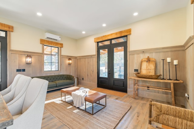 living room with french doors, light hardwood / wood-style flooring, an AC wall unit, and wooden walls