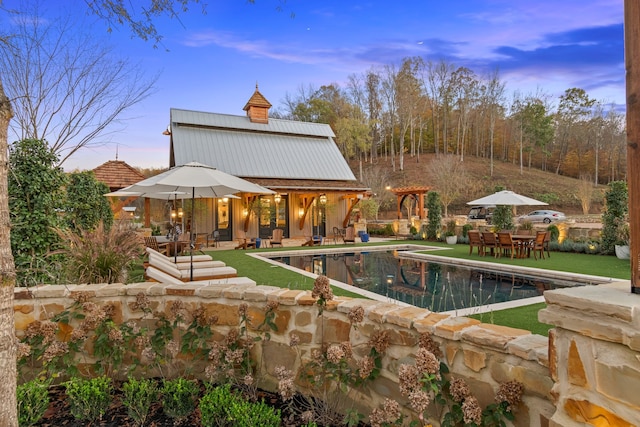 pool at dusk with a lawn, an outbuilding, and a patio