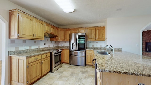 kitchen featuring sink, a brick fireplace, light stone countertops, appliances with stainless steel finishes, and kitchen peninsula