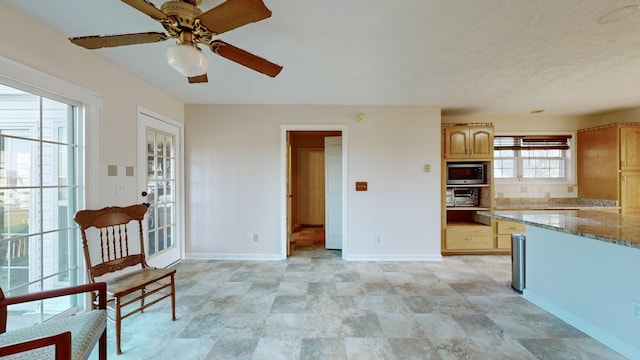 kitchen with light brown cabinetry, light stone countertops, stainless steel microwave, and ceiling fan