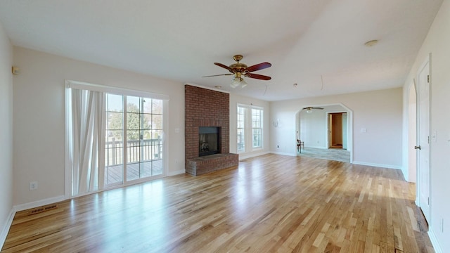 unfurnished living room featuring light wood-type flooring, a brick fireplace, a wealth of natural light, and ceiling fan