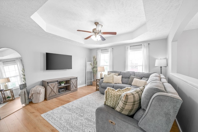 living room featuring hardwood / wood-style floors, ceiling fan, a textured ceiling, and a tray ceiling