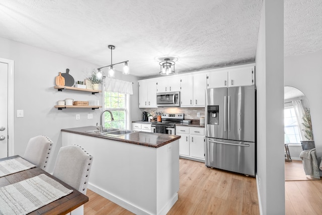 kitchen featuring kitchen peninsula, light hardwood / wood-style flooring, white cabinets, and stainless steel appliances