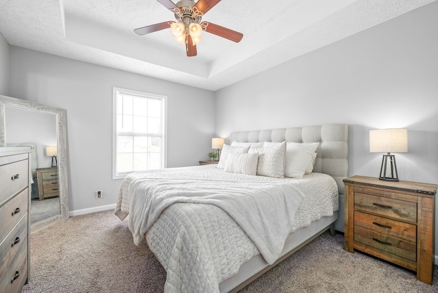 carpeted bedroom with ceiling fan, a textured ceiling, and a tray ceiling