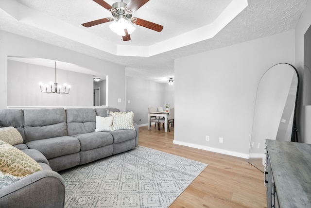 living room with a tray ceiling, light hardwood / wood-style flooring, ceiling fan with notable chandelier, and a textured ceiling