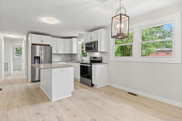 kitchen featuring stainless steel appliances, a healthy amount of sunlight, white cabinetry, a kitchen island, and hanging light fixtures