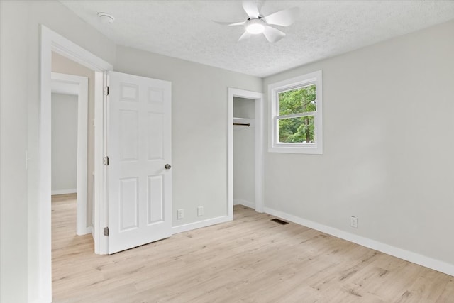 unfurnished bedroom featuring a textured ceiling, a closet, light hardwood / wood-style flooring, and ceiling fan