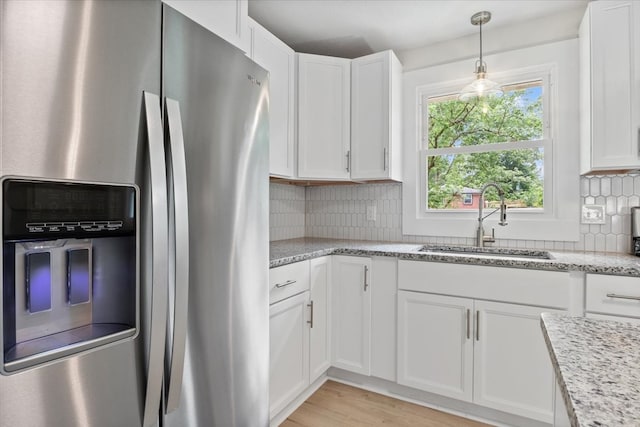 kitchen with white cabinets, sink, stainless steel refrigerator with ice dispenser, light stone countertops, and tasteful backsplash