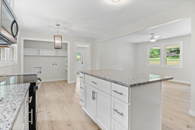 kitchen featuring light stone countertops, light wood-type flooring, pendant lighting, white cabinets, and a kitchen island