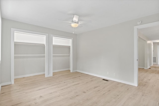 unfurnished bedroom featuring two closets, light hardwood / wood-style floors, and ceiling fan