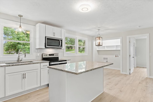 kitchen with stainless steel appliances, a healthy amount of sunlight, sink, a center island, and white cabinetry