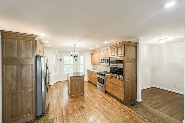 kitchen with stainless steel appliances, a center island, decorative light fixtures, and light wood-style flooring