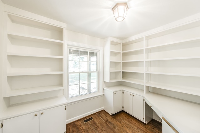 unfurnished office with dark wood-style floors, built in desk, and visible vents