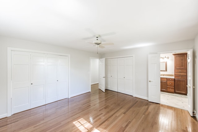 unfurnished bedroom featuring baseboards, ensuite bathroom, two closets, and light wood-style floors