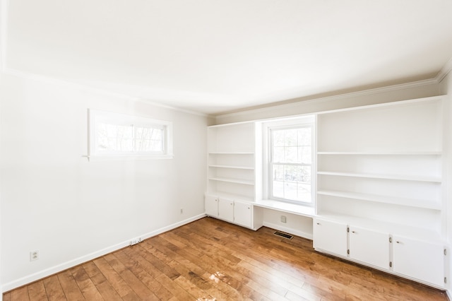 interior space with built in desk, visible vents, light wood-style flooring, ornamental molding, and baseboards