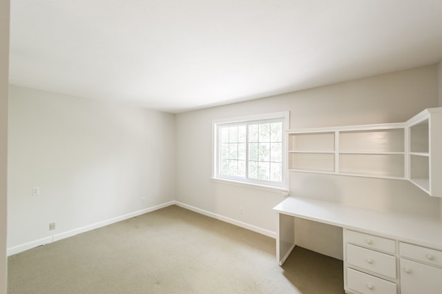 unfurnished office featuring baseboards, built in desk, and light colored carpet