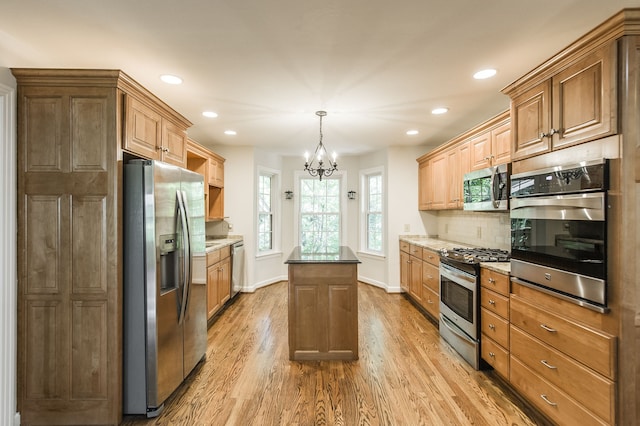 kitchen featuring decorative backsplash, a kitchen island, decorative light fixtures, stainless steel appliances, and light wood-type flooring