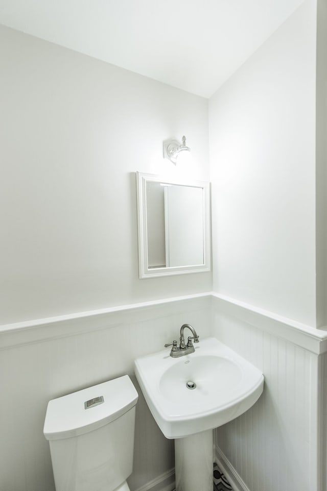 half bath with wainscoting, a sink, and toilet