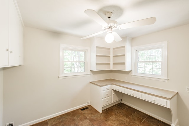 unfurnished office featuring a ceiling fan, a wealth of natural light, built in study area, and baseboards