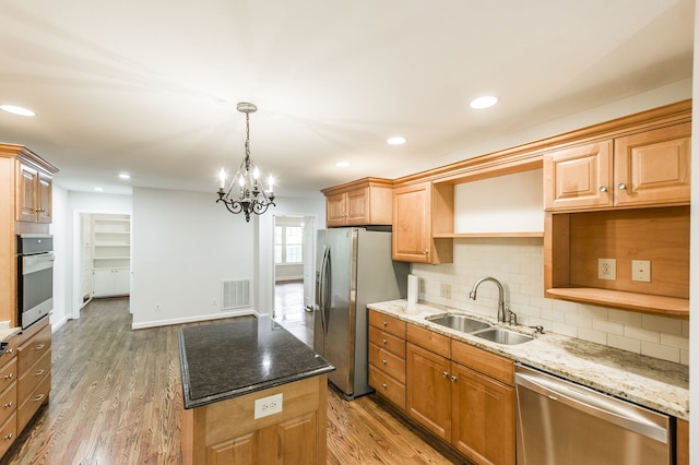 kitchen featuring dark stone counters, appliances with stainless steel finishes, wood finished floors, and a sink