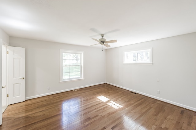 unfurnished room with ceiling fan, wood finished floors, visible vents, and baseboards