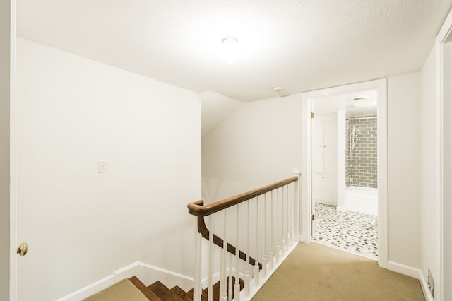 hallway featuring carpet floors, baseboards, a textured ceiling, and an upstairs landing