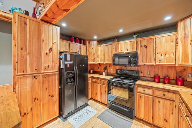 kitchen featuring light wood-type flooring, wooden walls, and black appliances