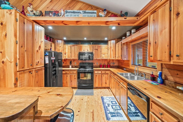 kitchen featuring sink, wood counters, vaulted ceiling, black appliances, and light wood-type flooring