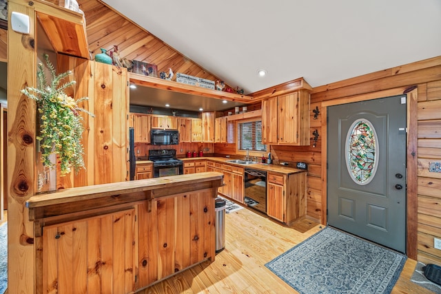 kitchen with sink, wood walls, light hardwood / wood-style floors, lofted ceiling, and black appliances