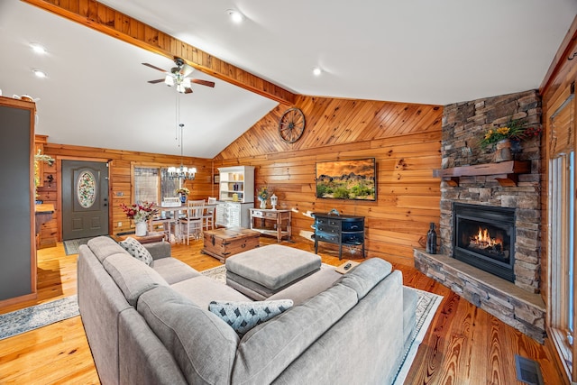 living room featuring vaulted ceiling with beams, wood walls, light wood-type flooring, and ceiling fan with notable chandelier