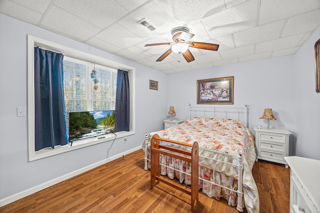 bedroom with ceiling fan, a drop ceiling, and wood-type flooring