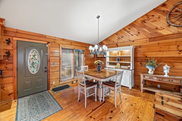 dining area with wooden walls, light hardwood / wood-style floors, vaulted ceiling, and an inviting chandelier