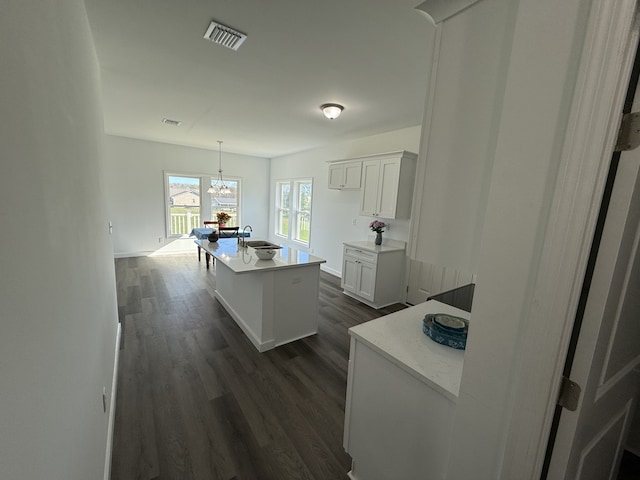 kitchen featuring pendant lighting, a kitchen island with sink, dark wood-type flooring, sink, and white cabinetry