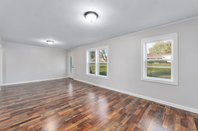 empty room with dark hardwood / wood-style flooring, plenty of natural light, and ornamental molding