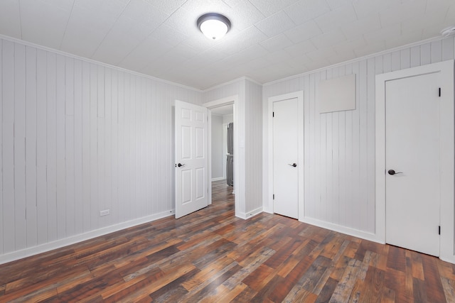 unfurnished bedroom with dark hardwood / wood-style flooring, crown molding, a closet, and wooden walls