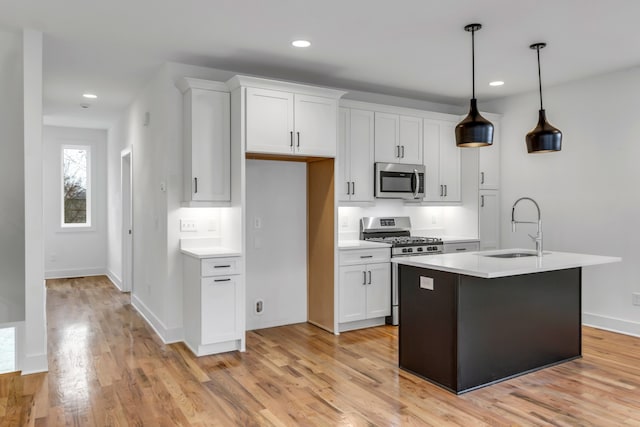 kitchen with white cabinetry, sink, hanging light fixtures, light hardwood / wood-style flooring, and appliances with stainless steel finishes