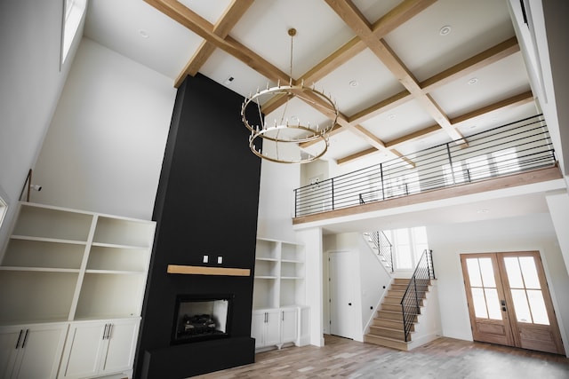 unfurnished living room featuring a high ceiling, coffered ceiling, an inviting chandelier, french doors, and light wood-type flooring