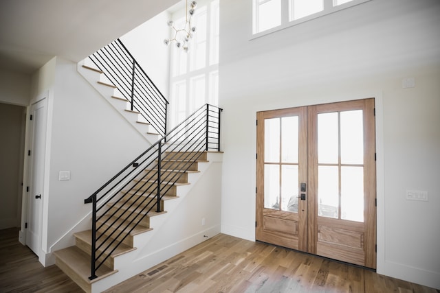 foyer with a wealth of natural light, french doors, a notable chandelier, and hardwood / wood-style flooring