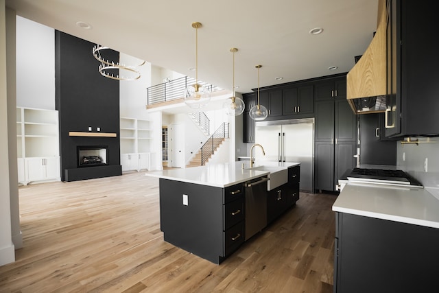 kitchen featuring stainless steel appliances, hardwood / wood-style floors, decorative light fixtures, a fireplace, and a center island with sink