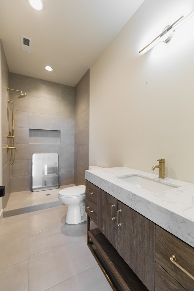 bathroom featuring tile patterned flooring, a tile shower, vanity, and toilet