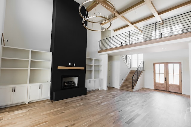 unfurnished living room with a large fireplace, french doors, coffered ceiling, a towering ceiling, and light wood-type flooring