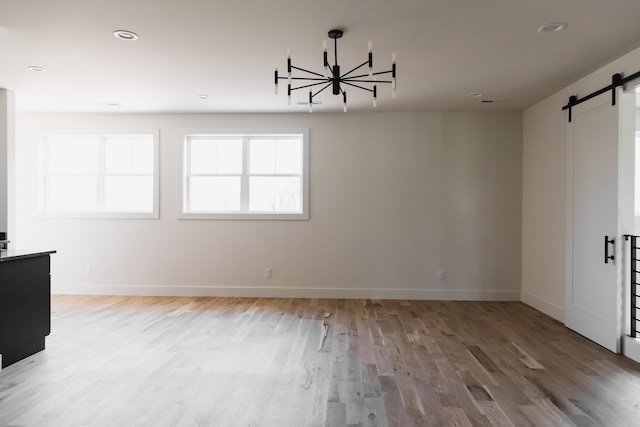 unfurnished room featuring hardwood / wood-style floors, a barn door, and an inviting chandelier