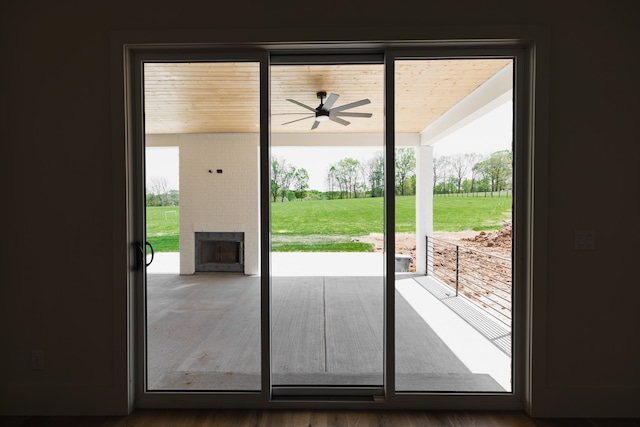 doorway with ceiling fan, a large fireplace, and hardwood / wood-style floors