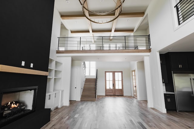 unfurnished living room featuring light hardwood / wood-style flooring, a high ceiling, and french doors