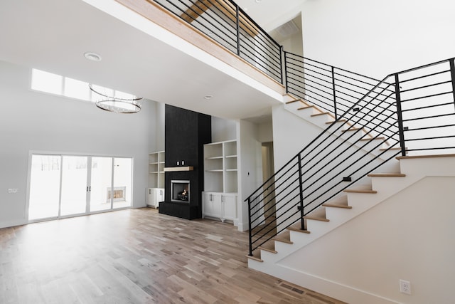 stairway featuring a fireplace, a towering ceiling, hardwood / wood-style flooring, and a notable chandelier