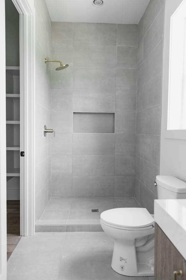 bathroom with tile patterned flooring, a tile shower, vanity, and toilet